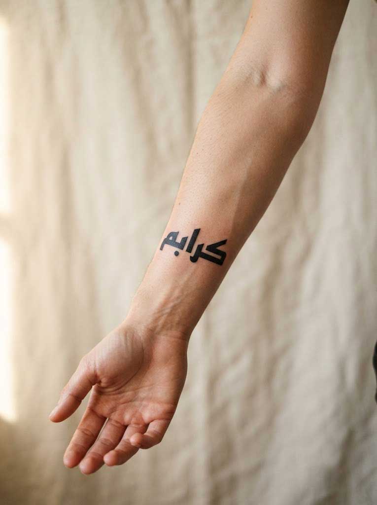 Mubarak (blessed) in Kufic Arabic calligraphy tattoo on forearm